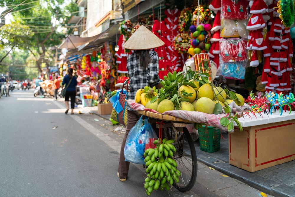 Kvinde cykler med varer til marked i Hanoi