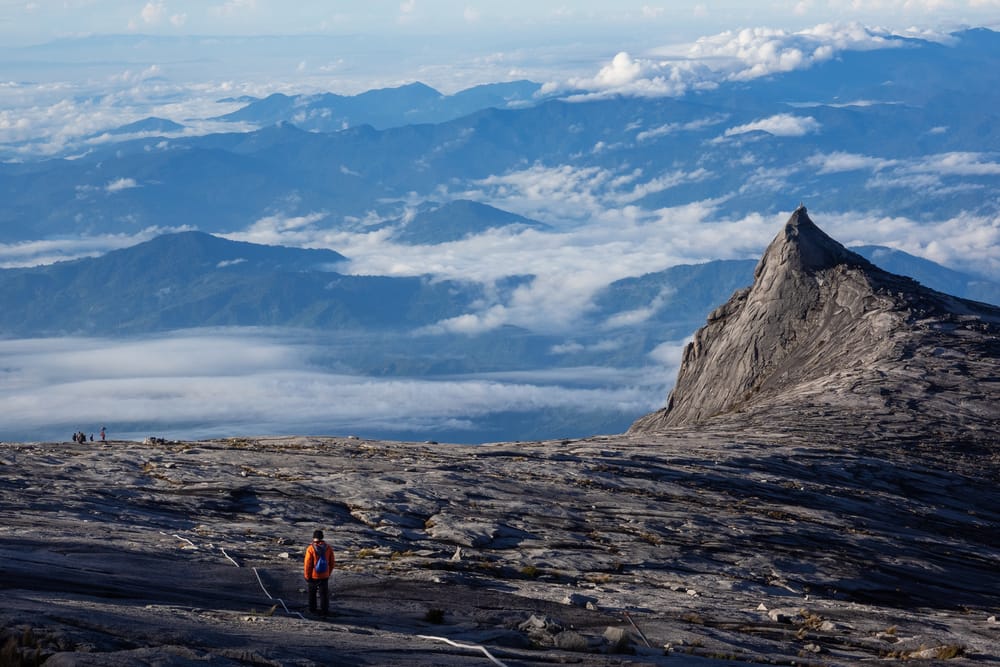 En vandrer står på Mount Kinabalu i det første gyldne morgenlys – et øjeblik af ro og storslået udsigt over skyerne på Borneo.