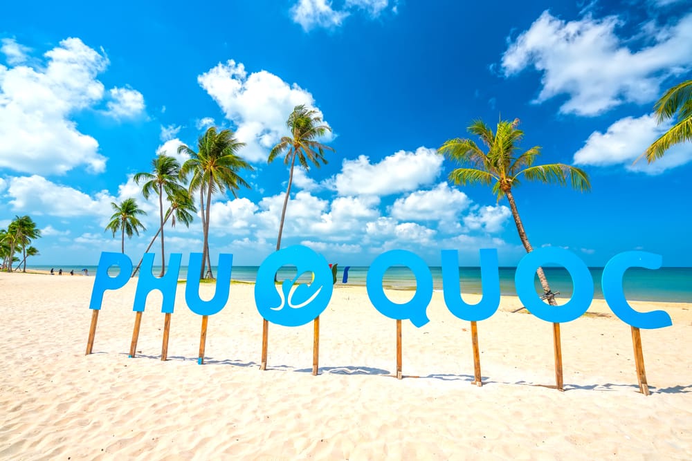 Tropisk strand med kokospalmer, hvidt sand og klart hav og Phu Quoc skilt på en solrig dag.