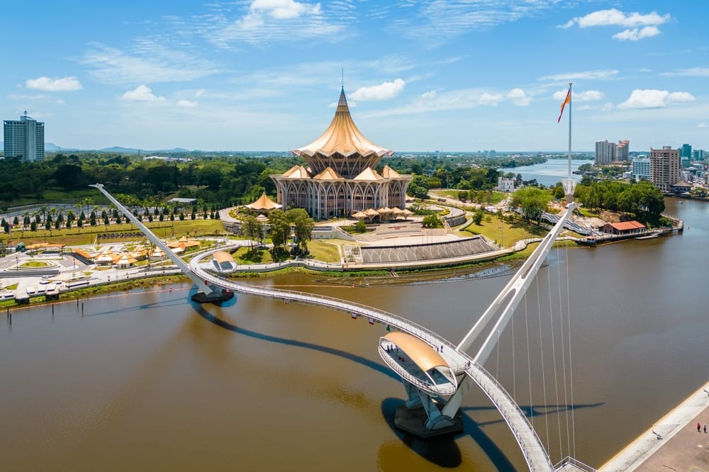 Udsigt over Sarawakflodens havnefront i Kuching, hvor lys, vand og traditionelle bygninger skaber en stemningsfuld atmosfære langs floden.