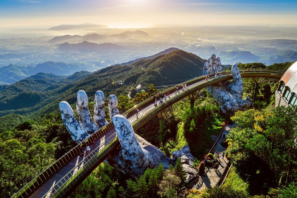 Turist går på Golden Bridge i Ba Na Hills, Da Nang, omgivet af bjerglandskab og gigantiske stenhænder.