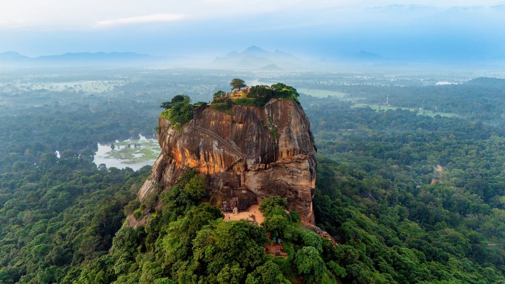 Sigiriya Rock Fortress set ved daggry, hvor klippen oplyses af varmt morgenlys omgivet af frodigt landskab.