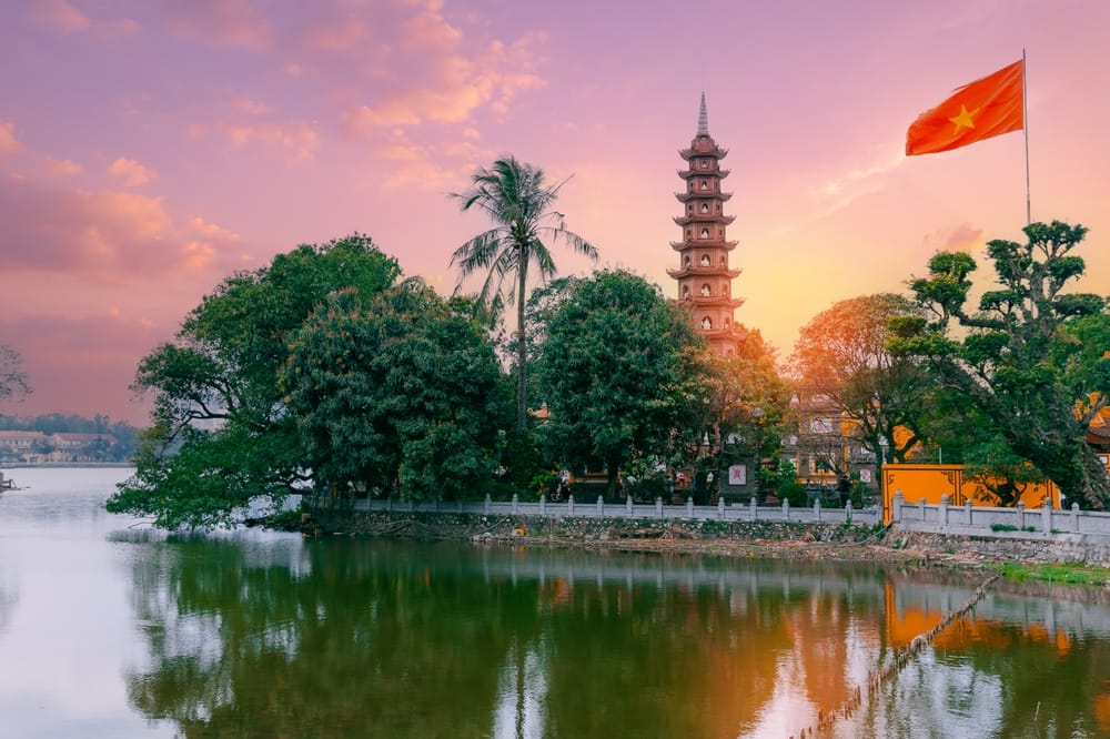 Tran Quoc-pagoden ved solnedgang i Hanoi, spejlende i West Lake med vietnamesiske flag