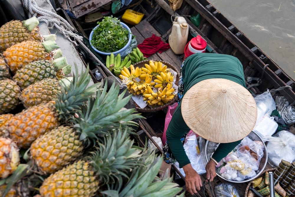Frugtsælger på en båd i Mekongdeltaet med tropiske frugter ombord i Vietnam