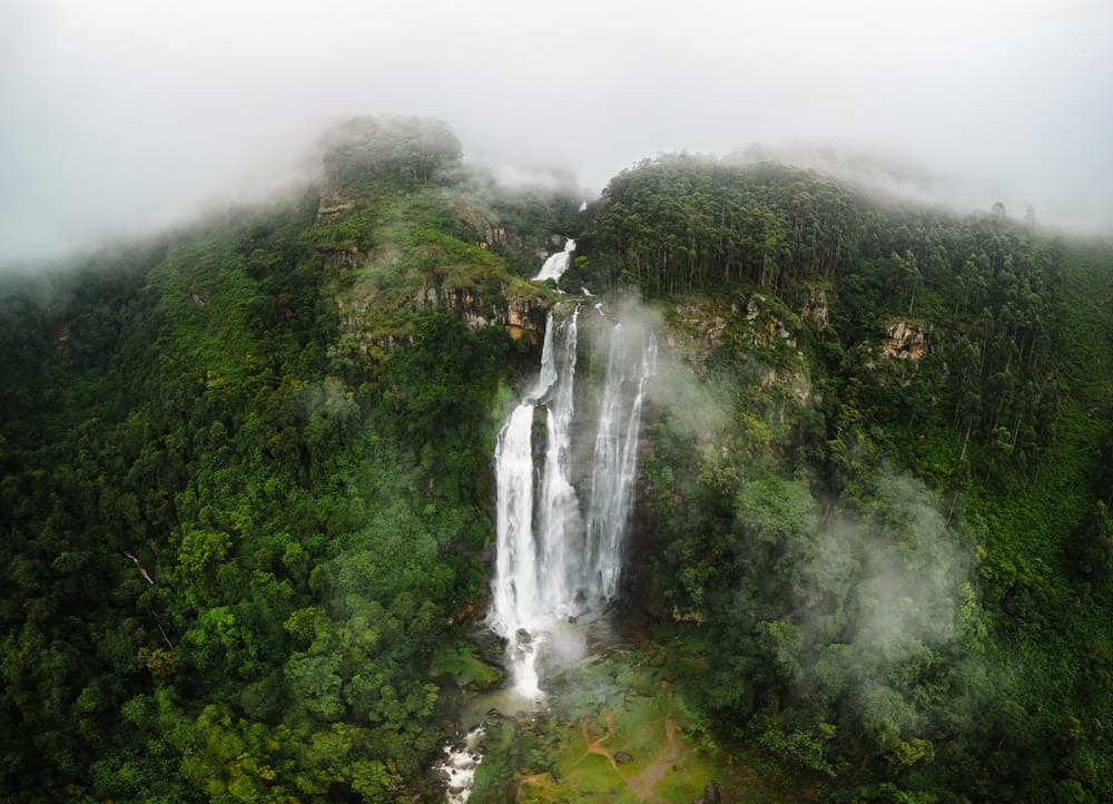 Dronefoto af Lover’s Leap-vandfaldet nær Nuwara Eliya, hvor vandet falder stejlt ned i grønne omgivelser.