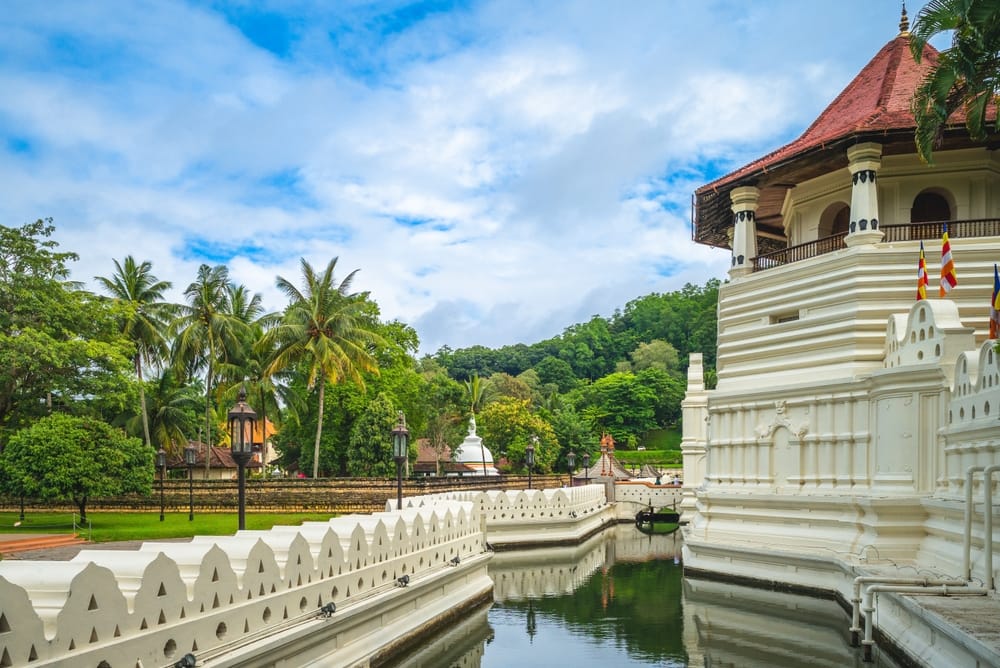 Temple of the Sacred Tooth Relic i Kandy med hvid tempelbygning, gyldne detaljer og besøgende i forgrunden.