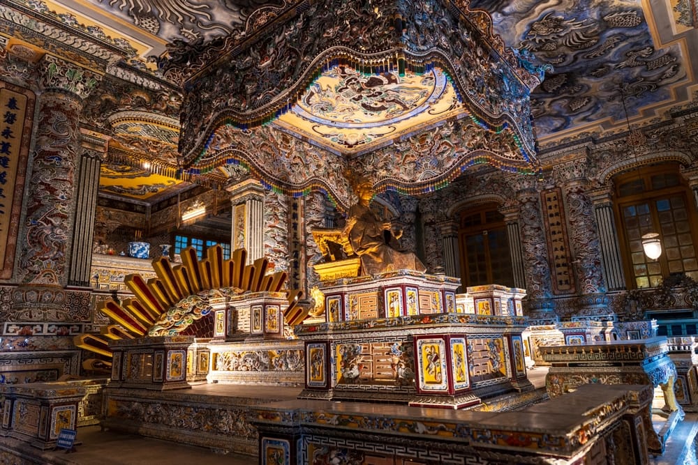 Interiør af Khai Dinh-mausoleet med farverige mosaikker og gylden statue af kejseren ved alteret.