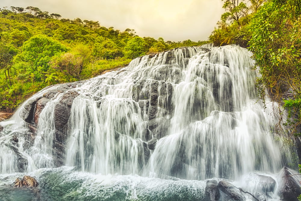 Et stemningsfuldt udsyn til Baker’s Falls i Horton Plains National Park hvor de kraftige vandstrømme breder sig ud over klipperne og skaber et smukt brusende vandfald midt i højlandets natur