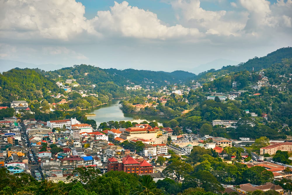 Panoramisk udsigt over Kandy i Sri Lanka med by, sø og grønne bjerge i baggrunden.