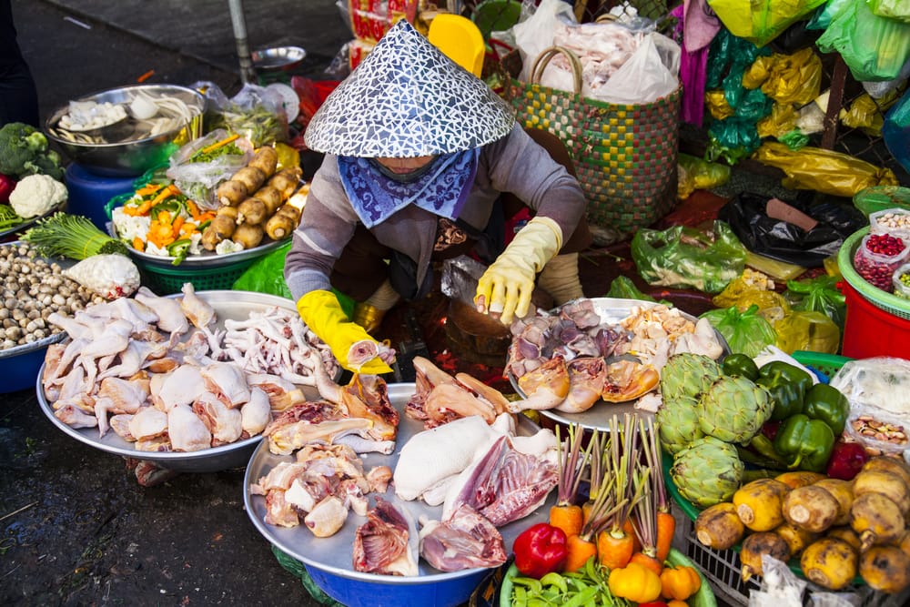 Lokal sælger i Ho Chi Minh City med friske råvarer på markedet, omgivet af farverige grøntsager og frugte