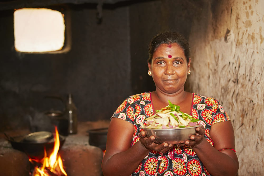 Kvinde tilbereder mad i et traditionelt køkken i Sri Lanka med enkle redskaber og åben ild.