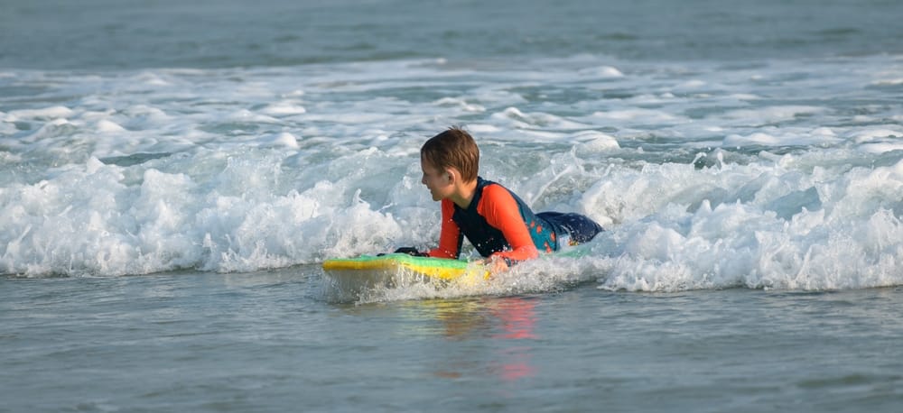 Ung dreng ligger på surfboard i havet ved Ahangama på Sri Lankas sydkyst med bølger og tropisk stemning.