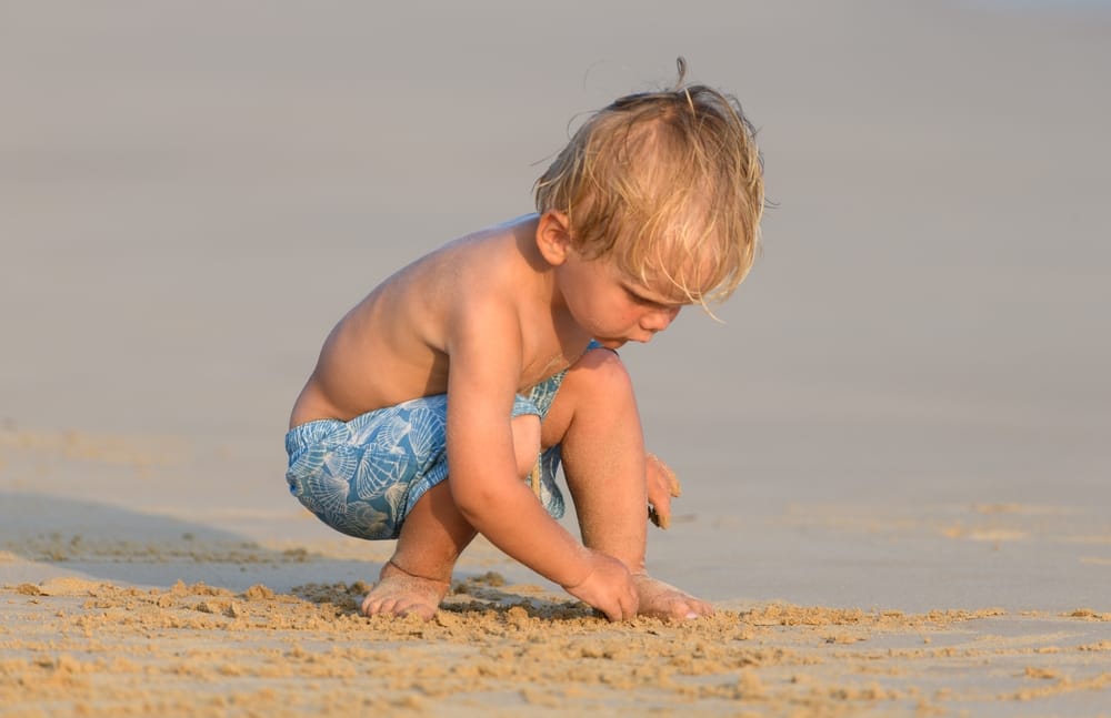 Lille barn leger på sandstranden i Ahangama på Sri Lankas sydkyst med Det Indiske Ocean i baggrunden.