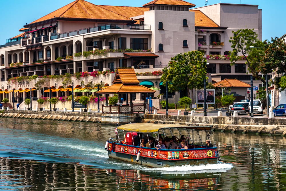 Båd med passagerer på Malacca River foran koloniale bygninger i Melaka.
