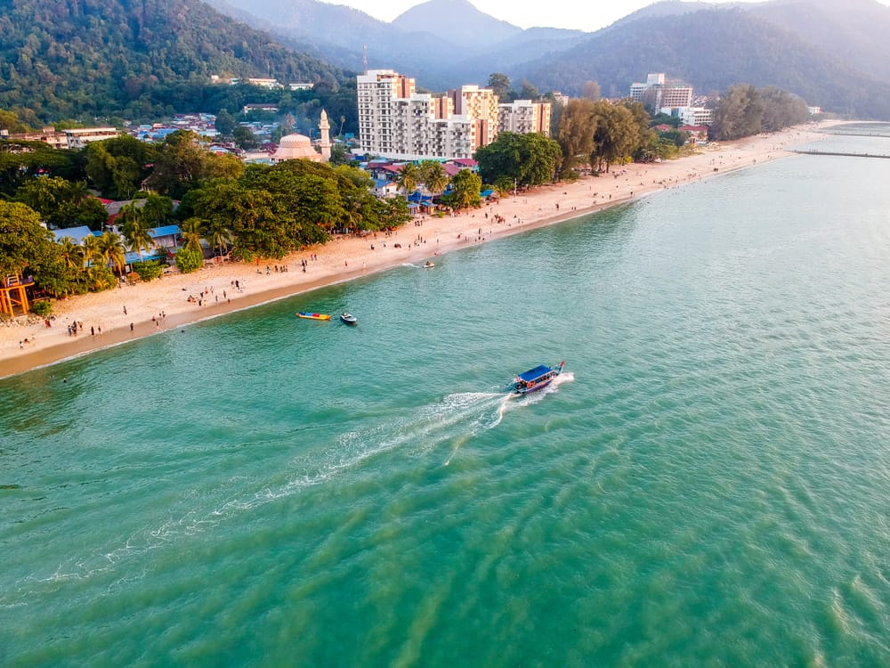 Luftfoto af Batu Ferringhi Beach på Penang med turkis hav, både og lang sandstrand.