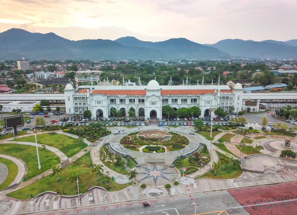 Ipoh Railway Station med hvid kolonial arkitektur og bjerge i baggrunden.