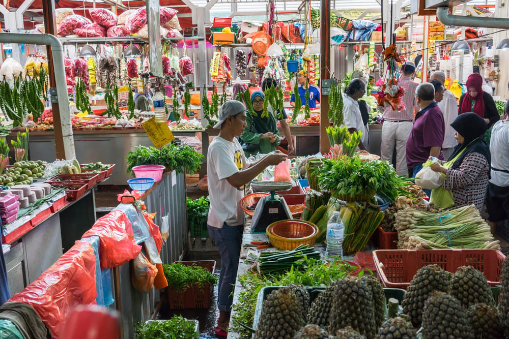 Lokalt marked i Malaysia med friske grøntsager, frugter og handlende mennesker.