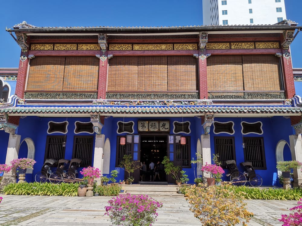Den blå Cheong Fatt Tze Mansion i George Town, Penang, med kolonial arkitektur, kinesiske detaljer og blomster i forhaven.