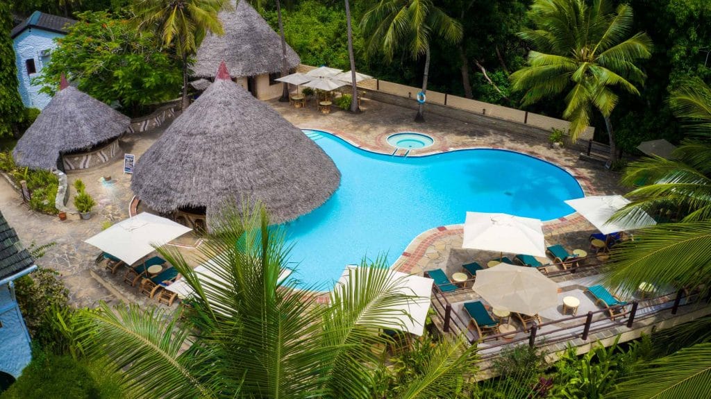Poolområde omgivet af palmer og stråtage på Pinewood Beach and Spa Resort i Kenya