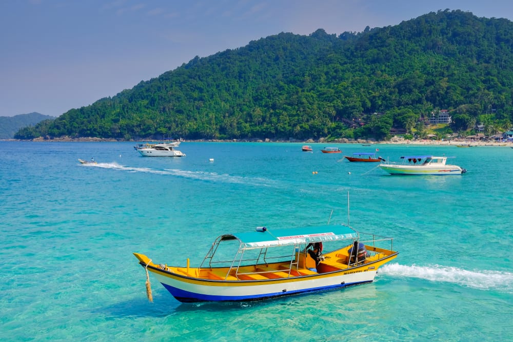 Farverige både sejler i det klare, turkise hav ved Perhentian Islands i Malaysia