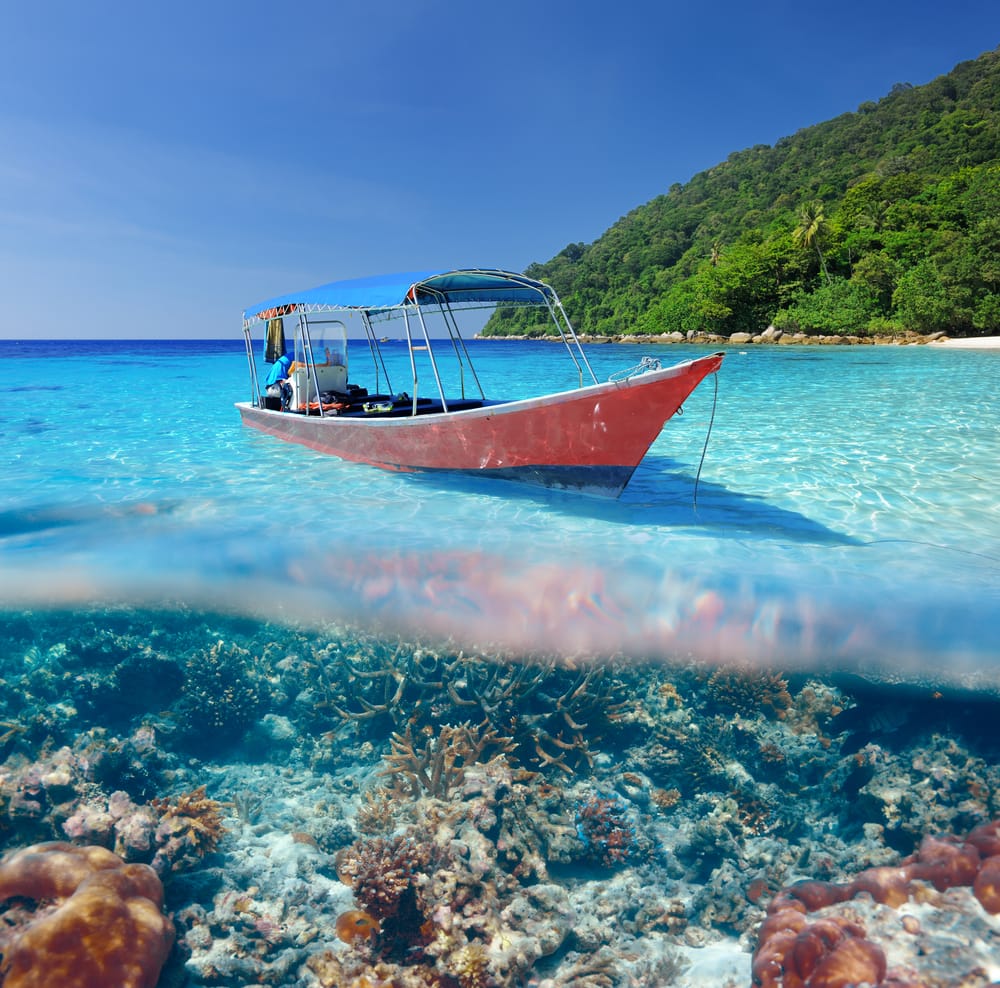 Lille båd i klart, lavt hav over koralrev ved Perhentian Islands i Malaysia