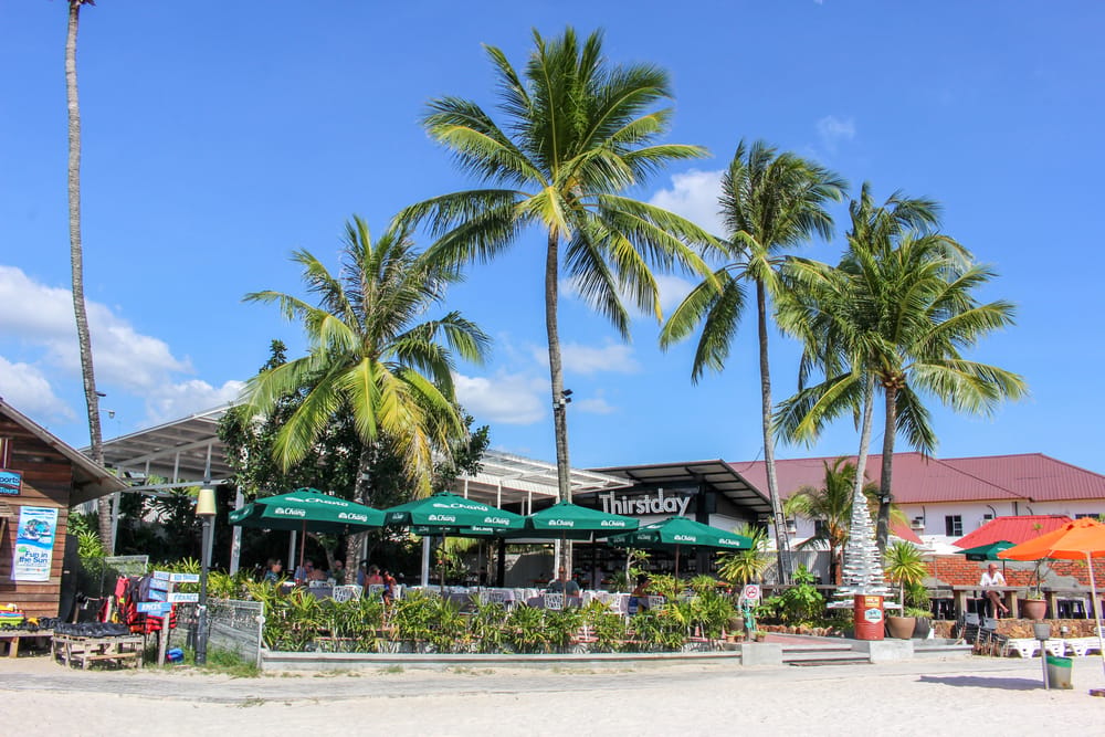 Palmer og strandcafé ved kysten i Langkawi med blå himmel og tropisk stemning.