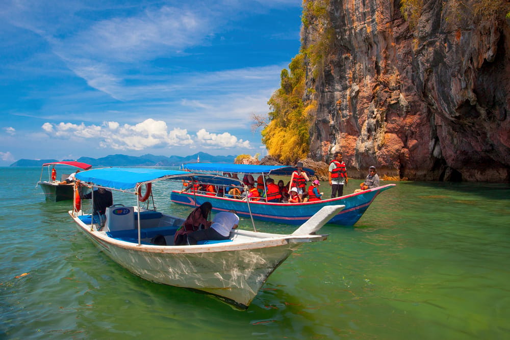 Turister i både med redningsveste ved kalkstensklipper under ø-hop i Langkawi, Malaysia.
