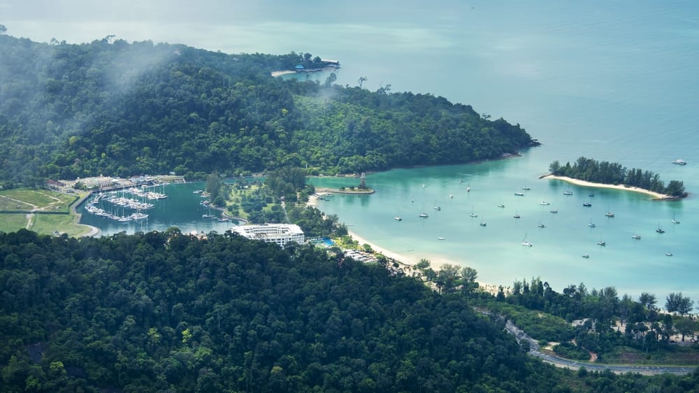 Luftfoto af tropisk bugt i Malaysia med grøn regnskov, hvid sandstrand og sejlbåde for anker i turkist vand.