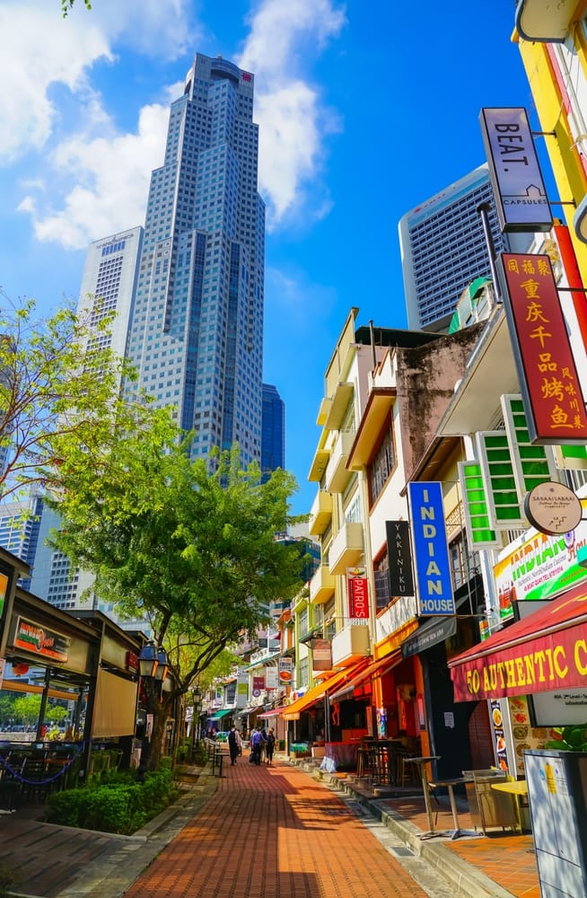 Farverige restauranter ved Boat Quay i Singapore med skyskrabere i baggrunden.