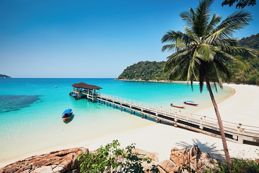 Hvid sandstrand med palmer og mole i det turkise hav ved Perhentian Islands i Malaysia