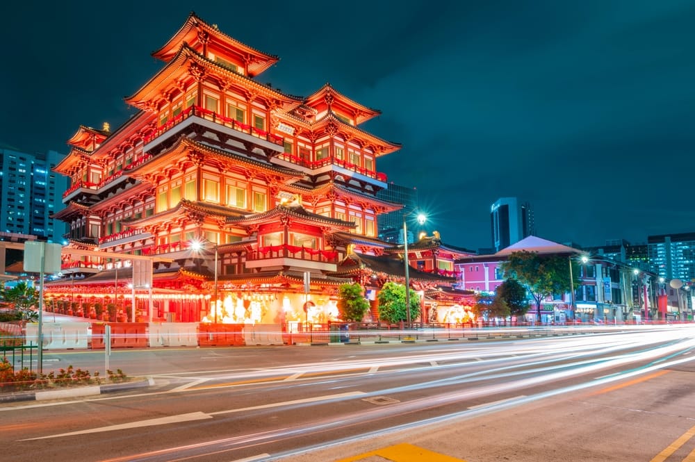 Buddha Tooth Relic Temple i Chinatown, Singapore, oplyst om aftenen med lysende facade og trafik i forgrunden.