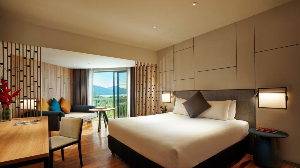 Hotel room with a king bed, seating area, and a window view of mountains and greenery.