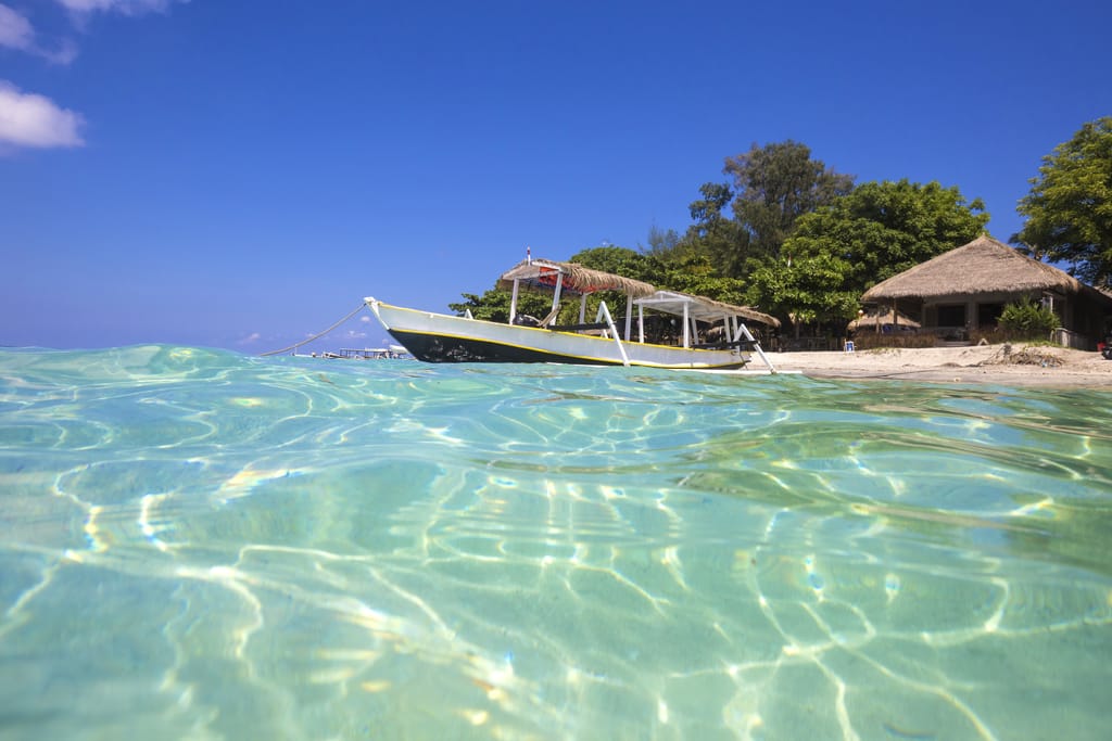 Longtailbåd på tropisk strand ved Gili Island, Bali – krystalklart hav og rolig østemning i Indonesien.