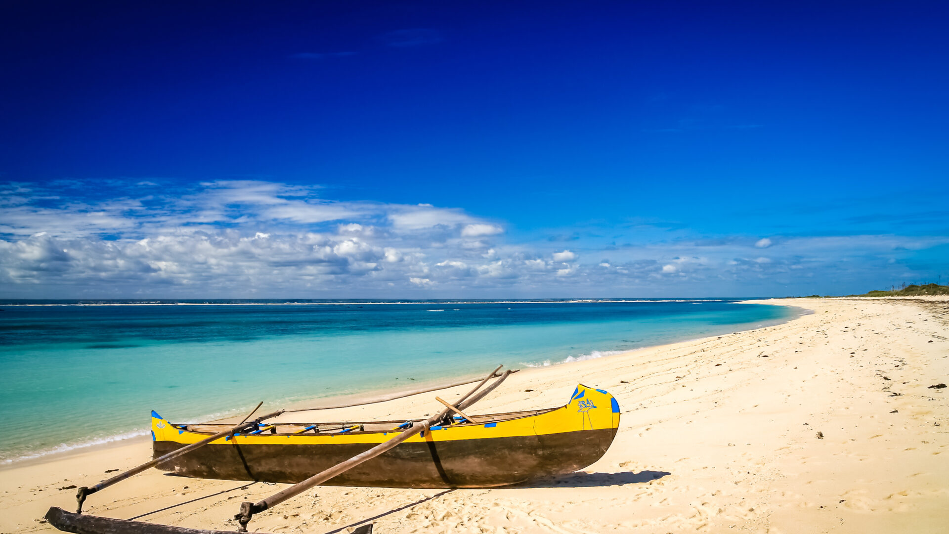 En lille traditionel pirogue hviler på sandstranden ved Nosy Ve Island, omgivet af Det Indiske Oceans blå nuancer.
