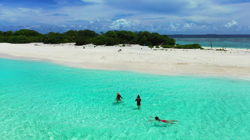 Gruppe af kvinder på stranden på Fulhadhoo-øen, Maldiverne – afslappet tropisk strandstemning med klart vand og hvidt sand.
