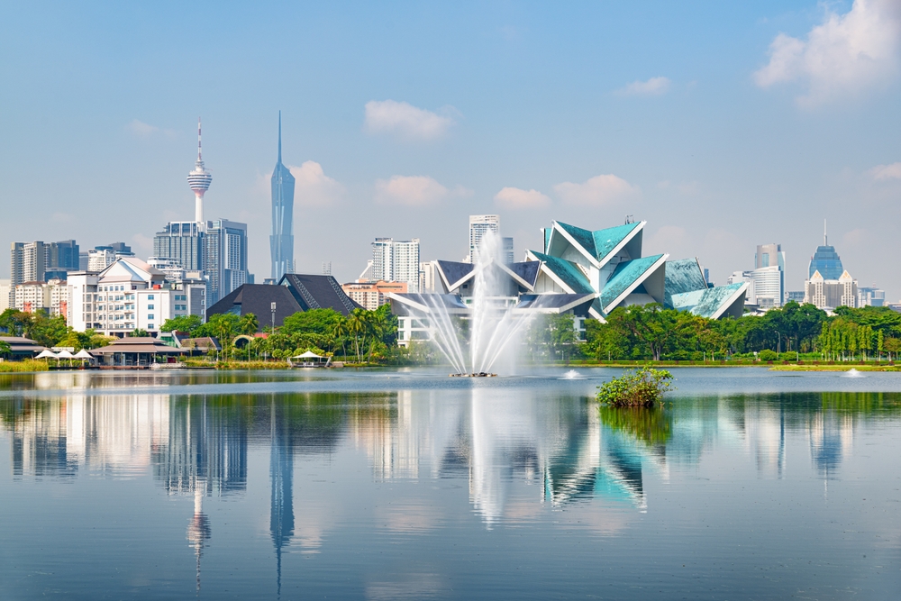 Udsigt over Kuala Lumpurs skyline med moderne højhuse spejlet i en naturskøn sø, hvor byliv og natur mødes