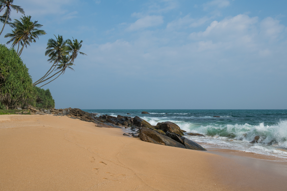 Tangalle Beach på Sri Lanka med store klipper, gyldent sand og turkisblåt hav under klar himmel.