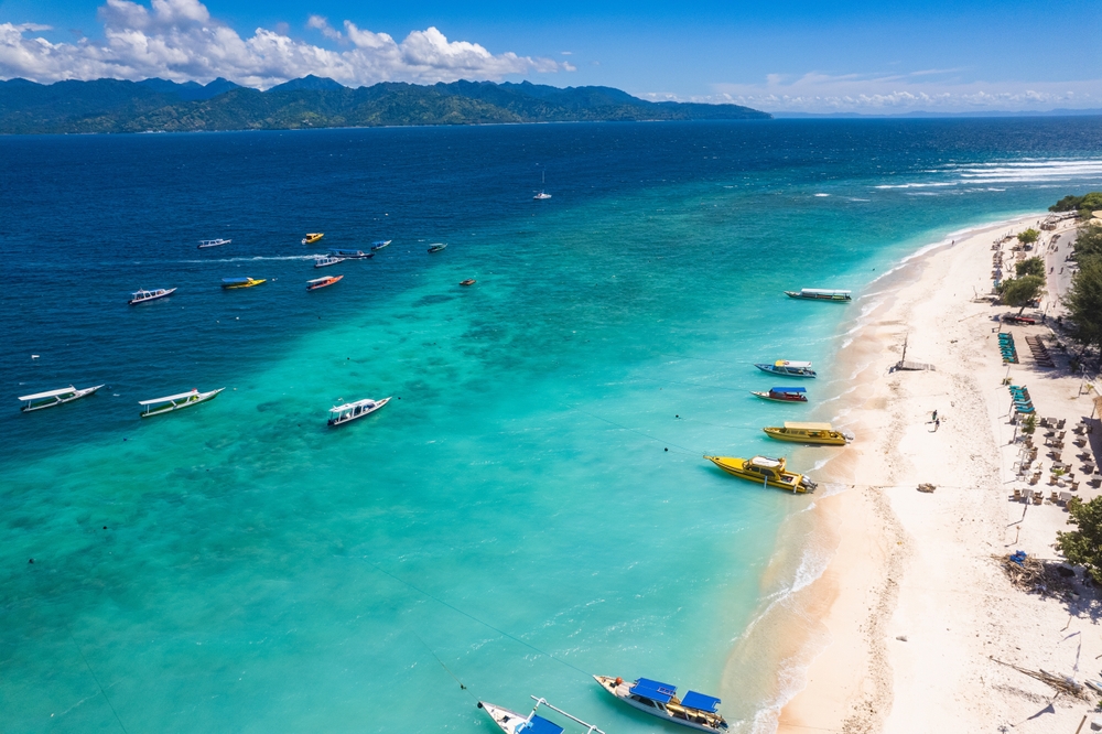 Gili Trawangan strand på Lombok, Indonesien, med hvidt sand, turkisblåt hav og palmer langs kysten.