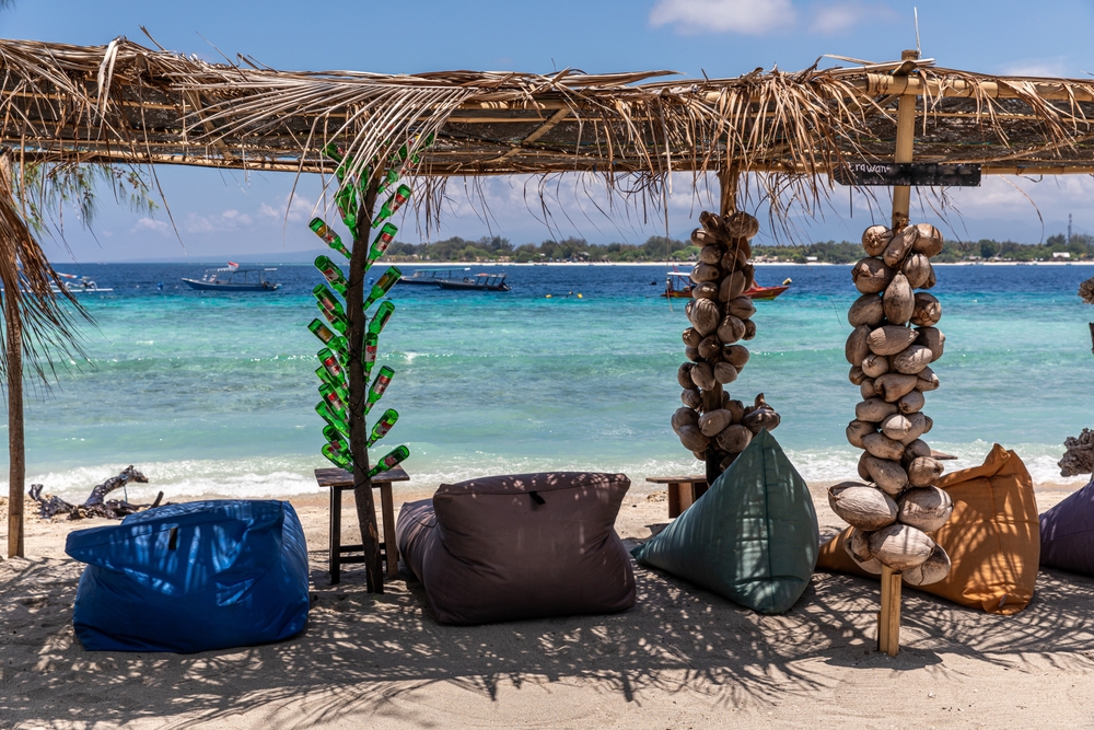 Solsenge på hvid sandstrand på Gili Trawangan, Indonesien, med palmer og turkis hav i baggrunden.
